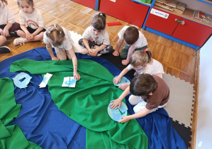 Dzieci układają puzzle z obrazkiem planety Ziemi.