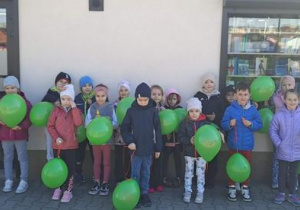 Na zdjęciu widzimy dzieci z grupy Motylki z balonikami pod Sklepem ze Zdrową Żywnością.