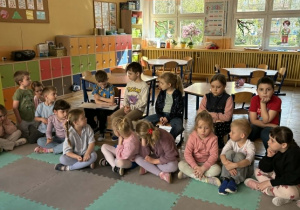 Dzieci siedzą na dywanie, słuchają bajki czytanej przez chłopca.