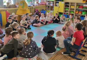 Dzieci siedzą na dywanie, słuchają bajki czytanej przez starszych kolegów.