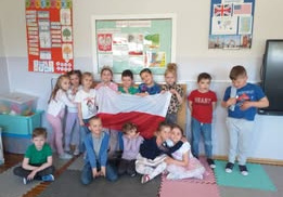1.2.Dzieci z grupy Odkrywcy pozują do zdjęcia z flagą Polski na tle kącika patriotycznego.