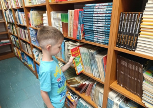 Chłopiec wybiera książkę, którą wypożyczy ze szkolnej biblioteki.