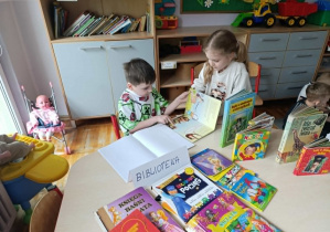 Dziewczynka i chłopiec z grupy „Misie” podczas zabawy w wypożyczanie książek.
