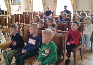 Dzieci siedzą na krzesłach w Muzeum Regionalnym czekając na lekcję muzealną.
