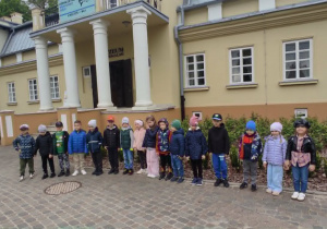 Dzieci pozują do zdjęcia stojąc na tle wejścia do Muzeum Regionalnego w Bełchatowie.