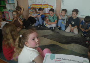 Dzieci siedzą na dywanie i słuchają opowiadania na temat Warmii i Mazur