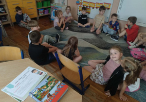 Zdjęcia przedstawia dzieci siedzące na dywanie słuchające o podróży do Krainy Tysiąca Jezior