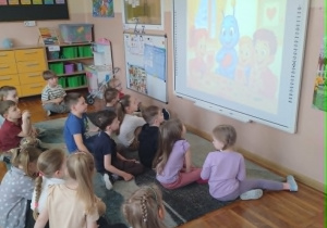 Zdjęcie przedstawia dzieci siedzące na dywanie które słuchają opowiadania Migotka o przyjaźni