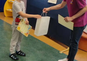 Nauczycielka wręcza chłopcu trzymającemu w dłoniach dyplom nagrodę za udział w konkursie.