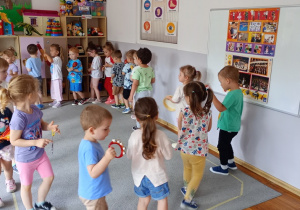 Dzieci chodzą w kole i grają na instrumentach muzycznych.