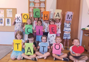 Dzieci trzymające kartki z napisem Kocham Cię Tato