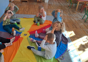 Dzieci podczas zabawy z chustą animacyjną i kolorowymi kubeczkami.