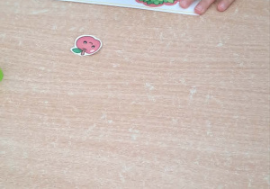 Dziecko przykleja jabłka na kartę pracy drzewka.