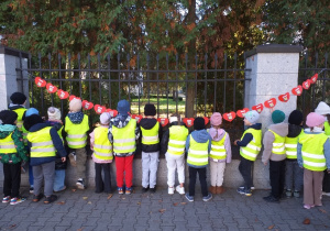 Dzieci z grupy Motylki wieszają łańcuch serc przy pomniku papieża Jana Pawła II.