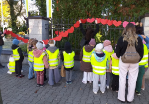 Dzieci z grupy Żabki wieszają łańcuch serc przy pomniku papieża Jana Pawła II.