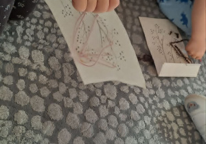 Dziewczynka przewleka włóczkę przez otwory w kartonowych szablonach.