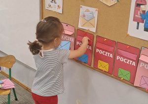 Dziewczynka umieszcza kopertę w skrzynce pocztowej o takich samych barwach.