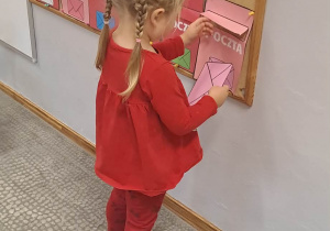 Dziewczynka wrzuca list do skrzynki pocztowej w tych samych kolorach.