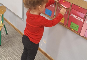 Dziewczynka nadaje list, umieszczając kopertę w skrzynce o tych samych kolorach.