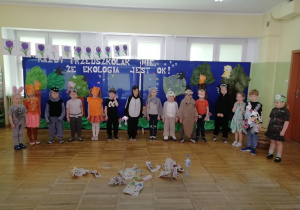 Grupa dzieci stojąca na tle dekoracji przedstawiającej las biorąca udział w przedstawieniu pt. „Przyjaciele natury”.