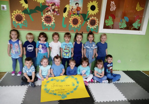 Ośmioro dzieci stoi a siedmioro siedzi przy ścianie ubrani w niebieskie koszulki i trzymają wykonany plakat w kształcie serduszka.
