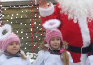 Dzieci w strojach aniołków pozuja do zdjęcia ze świętym Mikołajem.