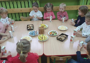 Dzieci siedzą przy stolikach, przed sobą mają przygotowany poczęstunek z okazji Mikołajek.