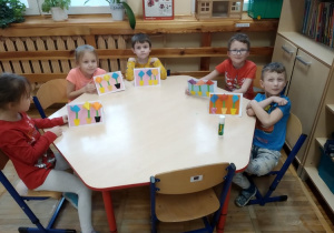pięcioro dzieci siedzi przy stoliku i pokazuje własnoręcznie zrobione kartki z kwiatkami.