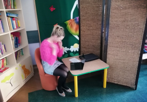Nauczycielka w różwowym sweterku odgrywa rolę Alicji cieszącej się z wiadomości na komunikatorze internetowymod nieznajomej koleżanki.