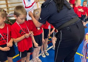 Pani Policjant zakłada medale na szyję naszym przedszkolakom, gratuluje przy tym sukcesu.