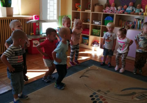 Grupa dzieci tańczy na dywanie.