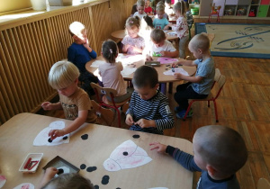 Dzieci siedza przy stoliku i naklejaja kropeczki na kształt biedronki.