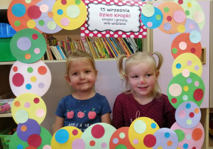 Dwie dziewczynki pozjka do zdjęcia w ramce wykonanej z kolorowych kropek.