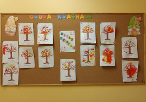Na tablicy wisi plakat z okazji Dnia Kropki oraz prace wykonane przez dzieci – jesienne drzewa z wystemplowanymi paluszkami kropeczkami, które mają kolory jesiennych liści.