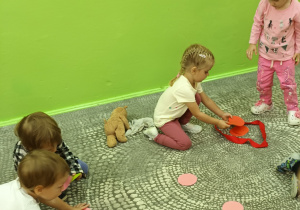 Dzieci na dywanie segregują rozrzucone koła w różnych kolorach pod względem kategorii zaproponowanych przez nauczyciela.