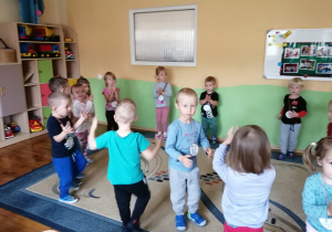 Gromada dzieci z medalami tańczy na dywanie.