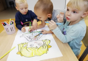 Trójka dzieci wspólnie koloruje obrazek przedstawiający dziewczynkę.