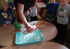 Nauczycielka wlewa sok jabłkowy do kubeczków do próbowania dla dzieci.