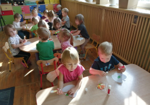 Dzieci wykonują prace plastyczne przy stolikach.