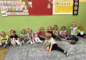 Grupa pozuje z czerwonymi opaskami jabłuszkowymi na tle dekoracji z okazji Dnia Jabłka.