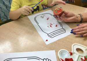 Dzieci stemplują połówkami jabłuszek pomalowanymi farbami na wydrukowanej sylwecie słoika.
