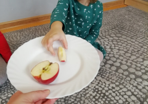 Dziewczynka w zielonej sukience częstuje się jabłkiem.