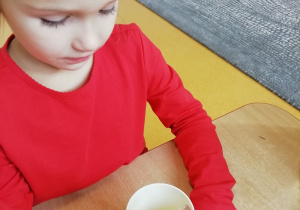 Dziewczynka w czerwonej bluzce pije sok jabłkowy.