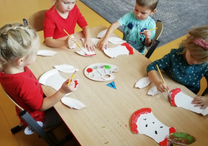 Dzieci siedzą przy stoliku i malują farbami papierowe ogryzki od jabłek.