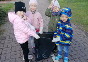 Dzieci trzymają worek na śmieci, zdjęcie z daleka.