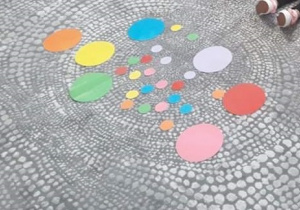Na szarym dywanie leżą różnokolorowe papierowe kropki