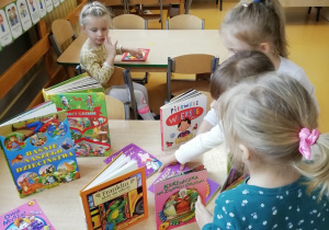 Dzieci oglądają książki rozłożone na stoliku.