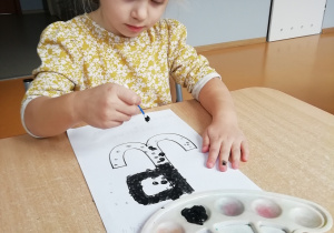 Dziewczynka wykropkowuje czarną farbą symbol Polski Walczącej.