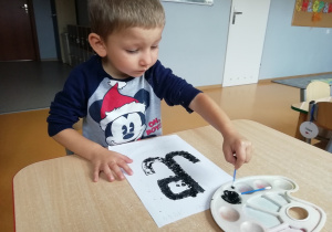 Chłopiec wykropkowuje czarną farbą symbol Polski Walczącej.