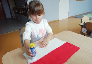 Dziewczynka przykleja białą bibułę do kartki.